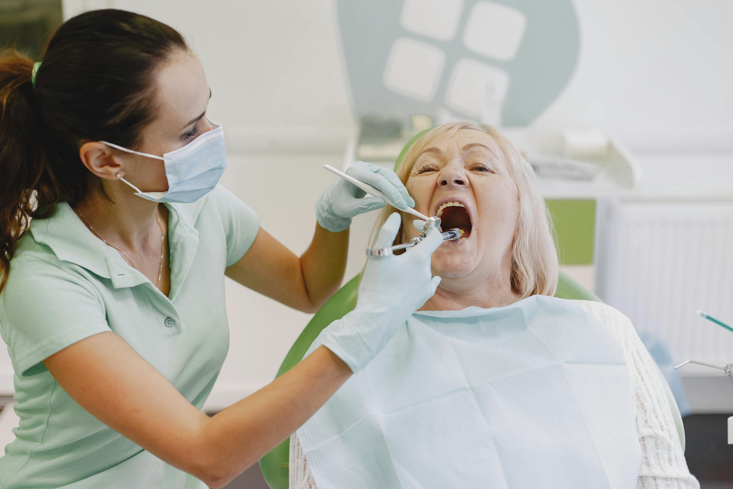 A female dentist examines a senior woman patient in a dental clinic setting.