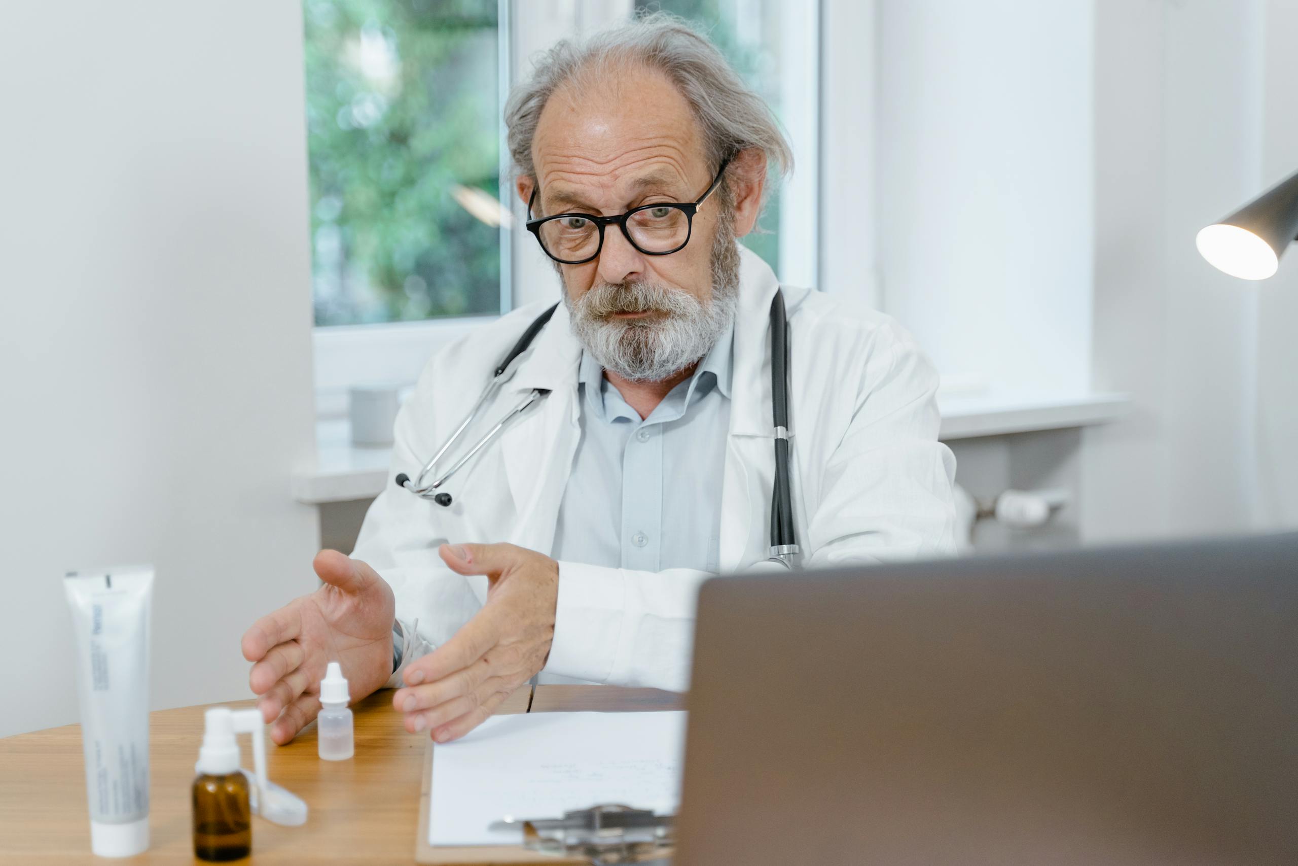 An elderly doctor in a white coat conducting an online medical consultation, focusing attentively.
