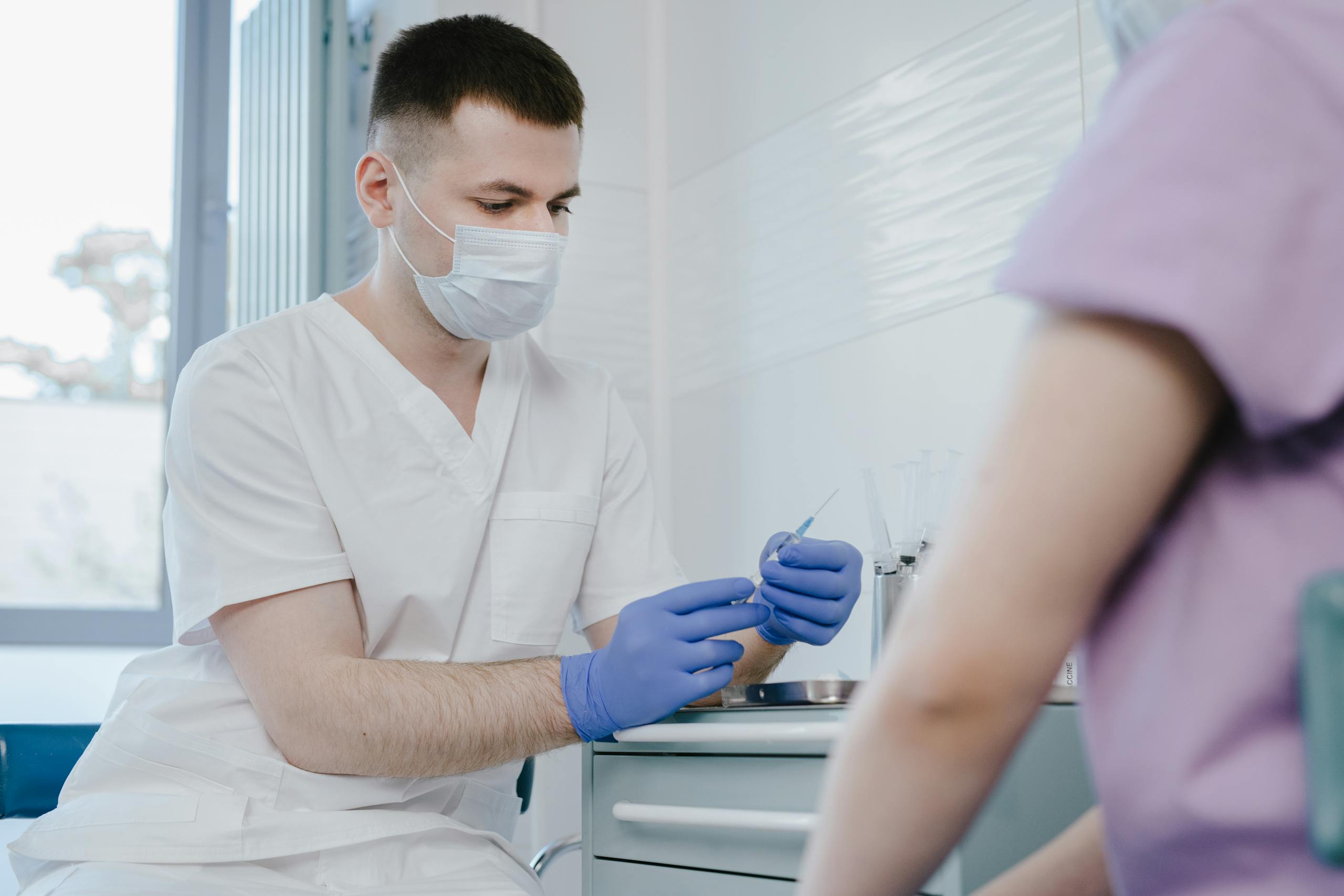 Healthcare worker in protective gear preparing a syringe for vaccination indoors.